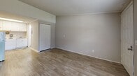 Located at 102 Hartford Run in Buford, GA, this single-floor unit offers a practical and well-organized layout comprising a living room, kitchen, and bathroom. The living room serves as the central space, featuring light wood-tone laminate flooring, neutral gray walls, and a textured ceiling. A large window allows natural light to fill the room, offering a view of the surrounding greenery, while a wall-mounted HVAC unit provides climate control. A closet adds functional storage to the living area. The kitchen is thoughtfully appointed with white cabinetry extending to the ceiling for ample storage, granite-look countertops, a white electric range, and a stainless steel sink. Under-cabinet lighting enhances the workspace, and the same laminate flooring carries through seamlessly. The bathroom maintains the clean, neutral aesthetic of the unit, with wood-look flooring, light gray walls, and crisp white fixtures. The overall design is cohesive and understated, with a bright, airy feel supported by a consistent light color palette throughout. This unit is well-suited for those seeking a straightforward, low-maintenance space in the Buford, GA area.