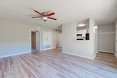 This 1-bedroom, 1-bathroom unit is designed with a practical, single-floor layout that maximizes functionality. The living room serves as the central gathering space, featuring light-toned wood-style flooring, neutral gray walls, and a ceiling fan with an integrated light fixture. A large sliding glass door floods the room with natural light while offering views of the outdoors. A pass-through opening connects the living area to the kitchen, enhancing the open feel of the space.

The galley-style kitchen is efficiently arranged with white cabinetry, granite-style countertops, white subway tile backsplash, and stainless or black appliances including a refrigerator, range, and dishwasher. Wood-style flooring continues throughout, and a door provides direct access to additional storage or entry areas.

The bedroom offers plush carpet flooring, a ceiling fan, and a closet with sliding panel doors. A separate walk-in closet with wire shelving provides additional storage capacity. A third closet is available elsewhere in the unit.

The bathroom includes a single vanity with mirror, a toilet, and a tub-shower combination with white subway tile surround. Wood-style flooring completes the clean, cohesive look throughout this well-organized unit.