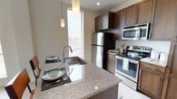 This single-floor residence offers a thoughtfully designed layout encompassing one bedroom and one bathroom. The kitchen serves as a central highlight of the space, showcasing rich dark-toned cabinetry that provides ample storage alongside a full suite of stainless steel appliances, including a refrigerator, range with oven, and built-in microwave. A granite-topped kitchen island anchors the space, doubling as a dining and prep area with an undermount sink and a high-arc contemporary faucet. The island comfortably accommodates seating for two, making it ideal for casual dining. Recessed lighting is complemented by elegant pendant fixtures that hang above the island, creating a warm and functional ambiance. A tall window adjacent to the kitchen allows natural light to fill the space, enhancing the clean, modern aesthetic. The overall design balances practicality with contemporary style, featuring neutral wall tones that complement the darker cabinetry and stone surfaces. The cohesive material palette and efficient use of space make this residence well-suited for comfortable everyday living.