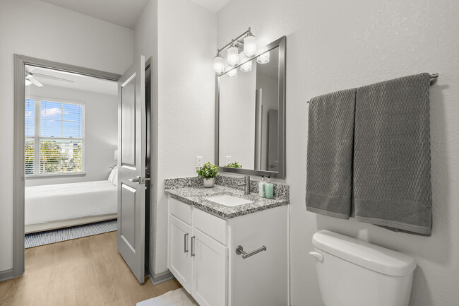 Bright modern bathroom with elegant granite countertop and view into a cozy, sunlit bedroom. - Avana Parkway