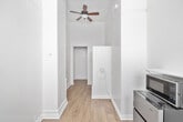 Located at 3942 8th Avenue in San Diego's vibrant Hillcrest neighborhood, this single-floor space offers a practical and efficiently designed layout comprising one bedroom and a hallway. The interior is finished in a clean, all-white palette that enhances the sense of openness throughout. Warm hardwood flooring runs continuously through both the hallway and bedroom, adding a natural, inviting contrast to the bright white walls and trim.

The hallway features built-in white shelving and bench storage, offering functional organization from the moment you enter. This passage leads directly into the bedroom, which benefits from two windows dressed with white horizontal blinds that allow for adjustable natural light. A ceiling fan with a light fixture is mounted overhead, providing both air circulation and supplemental lighting.

The bedroom also accommodates a compact appliance setup, including a stainless steel mini-refrigerator and microwave, along with a small white utility cabinet — making the space self-contained and practical. A wall-mounted shelf provides additional storage. The ceilings are notably tall, contributing to an airy feel that offsets the intimate footprint of the room. Overall, the space is clean, functional, and well-suited for a single occupant seeking a manageable, low-maintenance living environment in central San Diego.