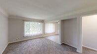 This single-story unit offers a well-organized layout with distinct living, dining, kitchen, and sleeping areas. The open living and dining space is a standout feature, with large windows dressed in vertical blinds that allow generous natural light and provide views of the surrounding greenery outdoors. Plush carpet flooring runs throughout the living and dining areas, creating a cohesive and comfortable feel. A ceiling fan is positioned in the dining area, adding a practical touch. Neutral-toned walls throughout contribute to a clean, bright ambiance.

The kitchen is efficiently designed and features white shaker-style cabinetry, stone-look countertops, and a full suite of stainless steel appliances, including a gas range, over-the-range microwave, and refrigerator. Tile-look flooring runs through the kitchen and into the bathroom, providing a durable, easy-to-maintain surface.

The bedroom is a well-proportioned room with carpet flooring, a window with vertical blinds, and a wide louvered bi-fold closet offering ample storage. The full bathroom includes a tub-shower combination with white tile surround, a vanity with white cabinetry, and tile-look flooring. The entry area provides additional closet access, rounding out the functional layout of the space.