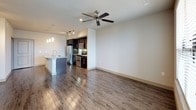 The Melrose floor plan offers a well-designed 2-bedroom, 1-bathroom layout on a single level, combining modern aesthetics with practical functionality. The open-concept living and kitchen area serves as the heart of the home, featuring rich dark wood cabinetry, granite countertops, a center island with a built-in sink, and a full suite of stainless steel appliances including a refrigerator with ice maker, range, and microwave. Pendant lighting and a track lighting system illuminate the kitchen, while wood-style flooring extends throughout the main living areas, adding warmth and continuity.

The living area is spacious and bright, with a ceiling fan overhead and a window providing natural light and outdoor views. Both bedrooms are carpeted for comfort and each feature ceiling fans, generous windows with horizontal blinds that invite natural light, and access to ample storage. A large walk-in closet with wire shelving on multiple levels offers exceptional organizational space.

The bathroom is finished with a dark-cabinetry vanity topped with granite, a large mirror, wood-style flooring, and a full soaking tub with shower. The overall design balances contemporary finishes with a clean, neutral palette, creating a cohesive and inviting living environment throughout.