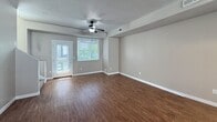 This 2-bedroom, 2-bathroom townhome offers 1,230 square feet of functional living space spread across three floors. The main living level spans 580 square feet and features an open-concept kitchen and living room with warm wood-style flooring and a ceiling fan. The kitchen is well-appointed with dark espresso cabinetry, dark granite countertops, black appliances including a gas range, built-in microwave, and refrigerator, plus a double sink and large windows that bring in abundant natural light. The living area is spacious with neutral gray walls and a ceiling fan with light fixture. A dedicated laundry room on this level includes a full-size washer and dryer. The upper floor encompasses 520 square feet and houses both bedrooms, including a primary bedroom of 170 square feet. Bedrooms feature plush dark carpet, neutral gray walls, and windows with blinds. Both bathrooms are finished with dark vanity cabinetry, gray countertops, single-basin sinks, large mirrors, and a tub/shower combination with wood-style flooring. Staircases connect all three levels, with the entry level contributing 130 square feet. The overall aesthetic is clean and modern with a cohesive neutral color palette throughout.