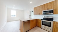 This thoughtfully designed single-floor unit showcases a contemporary aesthetic with clean lines and high-quality finishes throughout. The open-concept kitchen serves as the heart of the space, featuring warm wood-grain cabinetry, light quartz countertops, a peninsula with an integrated sink, and a full suite of stainless steel appliances including a refrigerator, electric range, microwave, and dishwasher. A decorative tile backsplash adds a refined touch. Light hardwood-style flooring flows seamlessly through the kitchen and into the adjacent living area, enhancing the sense of openness and continuity. Recessed lighting and a ceiling fan contribute to a bright, comfortable ambiance.

The unit includes two bedrooms, each finished with the same light flooring and equipped with a ceiling fan. Natural light enters through windows that overlook an exterior fence and deck area. Both rooms offer clean, neutral walls well-suited for a variety of uses.

Two bathrooms provide distinct experiences: one features a full soaking tub with white subway tile surround and chrome fixtures, while the other is appointed with striking marble-patterned tile flooring and walls, a glass-enclosed walk-in shower, and a modern vanity — adding a more elevated, spa-like feel to the space.