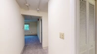 This two-bedroom, one-bathroom residence in Seabrook, New Hampshire, offers a straightforward single-floor layout designed for comfortable everyday living. The kitchen features light wood cabinetry, a tile backsplash, light wood-look vinyl plank flooring, and white appliances including a refrigerator, electric range, and dishwasher, with a entry door providing direct access. A peninsula counter adds a functional workspace and separation from the adjoining area. The living room is carpeted and includes a wide louvered bi-fold closet, providing generous storage. Both bedrooms are finished with soft carpet and neutral walls, each equipped with baseboard heating and windows overlooking lush greenery, filling the rooms with natural light. The primary bedroom features a wall-mounted air conditioning unit and a wide window, while the second bedroom includes its own louvered bi-fold closet. The full bathroom is accessed via the hallway and features wood-look flooring, a tub/shower combination, and clean white finishes throughout. A hallway connects all rooms efficiently, contributing to the unit's logical and accessible flow. Overall, the space presents a clean, functional, and well-organized living environment.