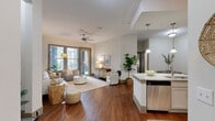 Located at 1701 N Lois Ave in Tampa, FL, this well-appointed 3-bedroom, 2-bathroom residence offers a thoughtfully designed single-level layout. The open-concept living, dining, and kitchen area serves as the heart of the home, where hardwood-style flooring flows throughout. The kitchen stands out with white shaker cabinetry, a decorative tile backsplash, granite countertops, stainless steel appliances, open display shelving, and a central island with pendant lighting and bar seating. The living room is bright and welcoming, featuring a ceiling fan, large windows, and a glass door that opens directly onto a private covered balcony, allowing for abundant natural light and outdoor views. The dining area provides an intimate space with clean lines and arched architectural detailing. The primary bedroom is generously sized, with plush carpeting, a ceiling fan, large windows with outdoor access, and a spacious walk-in closet with wire shelving. A second walk-in closet provides additional storage. Both bathrooms are finished with granite-topped vanities, gray shaker cabinetry, and tile flooring; the guest bath includes a full tub-shower combination. A dedicated in-unit laundry room with full-size washer and dryer adds everyday convenience to this well-rounded Tampa residence.