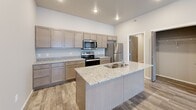 This thoughtfully designed 1-bedroom, 1-bathroom unit offers a functional and modern living experience across a single floor. The open-concept kitchen and living area serves as the heart of the unit, featuring wood-look plank flooring, recessed lighting, and a ceiling fan. The kitchen is well-equipped with taupe shaker-style cabinetry, granite countertops, a large center island with a dual-basin sink, and a full suite of stainless steel appliances including a refrigerator, electric range, and built-in microwave. The spacious living area receives natural light through a sliding glass door fitted with vertical blinds. The bedroom is carpeted for comfort, equipped with a ceiling fan, and features a window that allows in natural light. Two closets provide ample storage, including one generously sized walk-in closet with built-in shelving and hanging rods. The bathroom is clean and functional, offering a single-sink vanity with a large mirror, and a full shower-tub combo. Exposed ductwork visible in several rooms adds an industrial design element to the overall contemporary aesthetic of this well-laid-out unit.