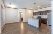 This single-floor residence offers a thoughtfully designed layout that balances open living areas with functional, well-appointed spaces. The living area is spacious and welcoming, featuring rich hardwood-style flooring, crown molding, and ceiling fans throughout. Multiple windows fitted with blinds allow natural light to fill the room, while an elegant arched passageway connects the living space to the rest of the unit, adding a refined architectural touch.

The kitchen is well-equipped with dark espresso-toned cabinetry, granite-style countertops, and a full suite of stainless steel appliances, including a refrigerator, range, and over-the-range microwave. A white subway tile backsplash provides a clean contrast to the rich cabinetry, and pendant lighting adds a polished finishing detail. The kitchen connects seamlessly to the main living areas, enhancing the open flow of the floor plan.

The bedroom is generously sized, featuring plush neutral carpeting, a ceiling fan, and dual windows that bring in ample natural light. The bathroom continues the design consistency of the unit, showcasing granite countertops, a dark wood vanity with an undermount sink, and a tub-shower combination.