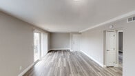 This well-appointed single-floor unit offers a clean, contemporary aesthetic throughout, highlighted by consistent luxury vinyl plank flooring in a warm wood-tone finish that flows seamlessly from room to room. Neutral greige walls and crisp white baseboards and trim create a cohesive, move-in-ready feel across the entire space.

The open living area is generously sized, bathed in natural light through a large sliding glass patio door fitted with vertical blinds, offering direct access to an outdoor area. A secondary window provides additional light and ventilation, further brightening the space.

The kitchen stands out as a functional centerpiece, featuring dark espresso-toned cabinetry with sleek bar-pull hardware, bright white countertops, and a full suite of stainless steel appliances including a refrigerator, electric range, over-the-range microwave, and dishwasher. A stainless steel sink with a modern gooseneck faucet completes the efficient layout.

The additional rooms are well-proportioned and versatile, each featuring the same durable flooring, neutral wall tones, and white trim. Windows with horizontal blinds allow for natural light while maintaining privacy. The unit also includes a private entry door, adding a sense of individuality and convenience to the overall layout.