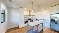 This well-appointed single-floor residence offers a smart and efficient layout across one bedroom, one bathroom, a kitchen, and a dedicated closet. The standout feature of the home is the kitchen, which showcases striking shiplap wall paneling, crisp white cabinetry, and granite-style countertops. A stainless steel appliance suite — including a gas range with a sleek wall-mounted hood, double oven, side-by-side refrigerator, and dishwasher — is complemented by open wood floating shelves and pendant lighting over a freestanding island with additional storage below. Warm hardwood-style flooring runs throughout the main living areas, adding a cohesive, contemporary feel. The bedroom is carpeted for comfort and features a ceiling fan and a large window framing outdoor views and abundant natural light. It connects conveniently to the walk-in closet, which is outfitted with wrap-around shelving and hanging rods, and to the full bathroom. The bathroom is finished with classic subway tile surrounding the tub and shower, a patterned penny-tile floor, a granite-topped vanity, and white cabinetry. The living area also features a ceiling fan, multiple windows, and a glass-panel entry door that enhances the open, airy character of the space.