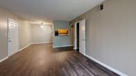 Located at 6502 Williamsburg Village Dr in Jackson, Tennessee, this single-floor unit offers a practical and well-organized layout throughout. The main living area greets you with rich, dark hardwood-style flooring and a ceiling fan overhead, creating a comfortable and inviting atmosphere. A six-panel entry door opens directly into the spacious living room, which flows seamlessly toward the kitchen via a pass-through counter opening. The kitchen is outfitted with warm oak cabinetry, dark laminate countertops, and a full suite of black appliances including a refrigerator, range, microwave, and dishwasher, all set atop matching hardwood-style flooring. The unit features multiple bedrooms, each finished with plush neutral-toned carpet, textured ceilings, and flush-mount lighting. One bedroom benefits from a window that invites natural light and outdoor views, while the others offer a cozy, enclosed feel. The bathrooms are well-appointed with oak vanities, gray countertops, large mirrors, and hardwood-style flooring, with one bathroom featuring a separate water closet for added privacy. Neutral taupe wall tones and white trim carry consistently throughout the space, contributing to a clean and cohesive aesthetic.