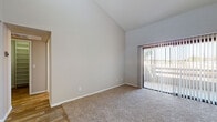 This single-floor residence offers a thoughtfully designed layout with a blend of comfort and modern updates throughout. The living area immediately impresses with its dramatic vaulted ceilings that amplify the sense of openness and volume. Large sliding glass doors fitted with vertical blinds flood the space with natural light and provide access to the outdoors. Plush wall-to-wall carpeting adds warmth underfoot, while wood-look flooring transitions seamlessly into the adjoining areas.

The kitchen is well-equipped and efficiently laid out in a galley style, featuring gray shaker-style cabinetry, white quartz countertops, a subway tile backsplash, and stainless steel appliances including a refrigerator, dishwasher, range, and microwave. Wood-look plank flooring runs the length of the kitchen, adding a clean, contemporary feel.

The bedroom is a comfortable, carpeted retreat with a ceiling fan, a vertical-blind window for natural light, and neutral tones throughout. A hallway leads to a walk-in closet with shelving, providing ample storage.

The bathroom features wood-look tile flooring, blue-gray vanity cabinetry with a white countertop and single sink, and a large mirror with overhead lighting, creating a bright and functional space. The overall aesthetic is clean, neutral, and move-in ready.