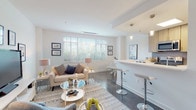 Located at 333 S Glebe Rd in Arlington, VA, this single-floor residence offers a thoughtfully designed open-concept layout with clean lines and contemporary finishes throughout. The living area is bright and welcoming, bathed in natural light from large windows with slatted blinds that frame views of surrounding greenery. Dark tile flooring anchors the space and flows seamlessly into the kitchen and dining areas.

The kitchen is a standout feature, equipped with stainless steel appliances, a gas range, a built-in microwave, and warm-toned wood cabinetry accented by a subtle tile backsplash. A generous white quartz breakfast bar with pendant lighting above serves as both a functional workspace and casual dining spot, while a dedicated dining area with a modern table and chairs sits adjacent.

The bedroom is a serene retreat with plush carpeting, crisp white walls, and ample natural light. A walk-in closet provides convenient storage, and the room's layout accommodates comfortable furnishings with ease. The bathroom features full-size tub and shower combination with tasteful taupe subway tile surround, light tile flooring, and a wood-toned vanity, delivering a clean, spa-inspired aesthetic. Every detail of this residence reflects a modern and functional design sensibility.