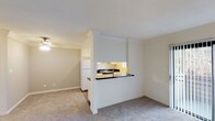 Located at 924 Encinitas Blvd #118 in Encinitas, this upstairs unit offers a well-organized, single-floor layout designed for comfortable everyday living. The living area is generously sized, featuring neutral-toned carpet, clean white walls, and a sliding glass door with vertical blinds that opens to a private outdoor space, allowing natural light to fill the room. A half-wall pass-through connects the living area to the kitchen, creating an open and communicative feel between spaces. The kitchen is efficiently designed in a galley style, showcasing white cabinetry that extends to the ceiling for ample storage, dark granite-style countertops, wood-look flooring, recessed lighting, a gas range, and a double-basin sink beneath a window. A full-size refrigerator completes the well-equipped space. The bedroom is a comfortable, carpeted room with a window overlooking greenery and a ceiling light fixture. The bathroom features wood-look flooring, white vanity cabinetry with dark countertops, a large mirror with overhead lighting, and a full tub-shower combination with tiled surround. The unit's consistent neutral palette and practical finishes throughout contribute to a clean, move-in ready atmosphere.