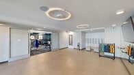 Located at 15024 North 90th Street in Scottsdale, Arizona, this well-appointed fitness and wellness facility spans a generous single floor, thoughtfully divided into two distinct functional areas. The space is defined by a clean, contemporary aesthetic, with crisp white walls, tray ceilings, and striking circular ring light fixtures that lend a modern, polished atmosphere throughout.

The main exercise room is outfitted with a comprehensive selection of cardio and strength-training equipment, including treadmills, recumbent bikes, ellipticals, cable machines, and weight benches. Patterned carpet flooring adds texture and warmth, while blue accent walls decorated with framed artwork and a classic wall clock create an energizing yet refined environment. Natural light filters in through large windows, offering views of the surrounding outdoor spaces.

Adjacent to the gym is a spacious open studio featuring smooth luxury vinyl flooring, floor-to-ceiling mirrors, a wall-mounted television, and direct access to an outdoor patio through glass doors. Built-in cabinetry and storage racks for fitness accessories keep the space organized and functional. Circular pendant lighting continues the design language from the gym, tying the two areas together cohesively. The facility also connects to a grand lobby area, featuring soaring ceilings, a statement fireplace, and elegant arched windows, enhancing the overall sense of openness and sophistication.