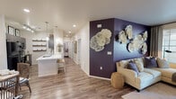 Located at 8855 N Casa Grande Hwy in Marana, Arizona, this single-floor residence offers a well-designed layout that balances comfort and style throughout. The open-concept living area makes a striking impression with rich wood-look flooring, recessed lighting, and a bold deep-purple accent wall adorned with sculptural wall art, creating a memorable focal point. The space flows seamlessly into the kitchen, which features dark cabinetry with modern hardware, a white quartz peninsula with bar seating, open shelving, pendant lighting, and black appliances. An adjacent dining nook benefits from natural light through window blinds and is accented by decorative lattice wall panels. The primary bedroom offers direct access to a private balcony via sliding glass doors, providing outdoor living space with community views. Additional bedrooms include a cozy carpeted room with a ceiling fan and natural light, as well as a creatively designed room featuring a bold gold-patterned accent wall. The bathrooms are finished with wood-look flooring, white quartz countertops, and dark or neutral cabinetry, offering a clean and contemporary aesthetic. Throughout the home, a cohesive neutral palette is punctuated by thoughtful design details, making this Marana residence both functional and visually engaging.