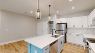 Located in Calabash, NC, this 3-bedroom, 2-bathroom single-floor home offers a well-designed layout with modern finishes throughout. The kitchen is a standout feature, showcasing crisp white shaker cabinetry with matte black hardware, a classic subway tile backsplash, quartz countertops, and a distinctive light blue center island with an integrated sink and pendant lighting overhead. Stainless steel appliances, including a full-size refrigerator and microwave, complement the space, while an open walk-in pantry provides generous storage. Light wood-look flooring flows through the main living areas, adding warmth and continuity. The living room benefits from abundant natural light and direct access to a private balcony through sliding glass doors, offering pleasant outdoor views. The spacious primary bedroom features its own sliding glass door to the balcony, a ceiling fan, and light hardwood flooring. The two additional bedrooms are finished with plush carpeting, ceiling fans, and windows that bring in natural light. Both bathrooms are clean and functional, featuring tub/shower combos with white surrounds. Two closets provide practical storage throughout the home, completing this thoughtfully arranged residence.
