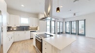 This well-appointed single-floor residence offers two bedrooms and two bathrooms within a thoughtfully designed open layout. The kitchen serves as a central focal point, featuring a large island with a built-in cooktop, stainless steel appliances including a French door refrigerator, white shaker cabinetry, a gray tile backsplash, and a statement overhead range hood. Pendant lighting and recessed fixtures illuminate the space, while light hardwood flooring extends throughout the main living areas.

The kitchen flows seamlessly into the living area, which benefits from an abundance of natural light provided by floor-to-ceiling windows offering outdoor views. A ceiling fan overhead adds functional comfort to this bright, open space.

The primary bedroom is generously proportioned, featuring large windows with exterior views and a dedicated bathroom finished with dual granite-topped vanities, white cabinetry, and a glass-enclosed tub and shower combination. A walk-in closet with built-in shelving connects directly to the primary bathroom. The second bedroom features plush carpeting, a ceiling fan, and a window with exterior views. Clean white walls and modern gray-accented doors unify the overall aesthetic throughout.