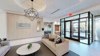Located at 80 Mill St in Hanover, Massachusetts, this single-floor community amenity space offers a generously sized, thoughtfully designed environment suited for socializing, relaxation, and gathering. The interior showcases a cohesive contemporary aesthetic, anchored by light-toned herringbone-patterned flooring that flows throughout the open layout, creating a seamless visual continuity from room to room.

The main living area serves as the heart of the space, featuring a striking floor-to-ceiling herringbone tile accent wall with a sleek, linear gas fireplace as its centerpiece. Adjacent to this focal point is a games area complete with a full-size billiards table, set atop a neutral area rug beneath recessed lighting. A built-in media wall with light wood cabinetry, a large flat-screen television, and integrated shelving provides a dedicated entertainment zone.

A separate lounge and dining area is distinguished by rich pendant lighting, warm wood accents, and a gas fireplace with a dark tile surround, offering a more intimate atmosphere. Large glass doors in this wing invite natural light and views of the outdoor surroundings. The entry lobby features floor-to-ceiling glazing, sheer drapery panels, and comfortable lounge seating, creating a welcoming transition into the space. Throughout, white ceilings, recessed lighting, and clean architectural lines reinforce the modern, refined character of this well-appointed facility.