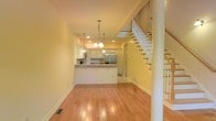 This two-story home offers a well-designed layout that blends functionality with classic charm. The main level centers around an open-concept living and kitchen area, where warm hardwood flooring flows seamlessly throughout the space, creating a cohesive and inviting atmosphere.

The kitchen is equipped with white raised-panel cabinetry, granite countertops, and stainless steel appliances, including a full-size refrigerator. A peninsula with an overhang provides casual bar-style seating and serves as a natural divider between the kitchen and the living area. Pendant lighting and a multi-light chandelier hang above the peninsula, adding both task lighting and decorative appeal. Recessed lighting throughout the ceiling further enhances the brightness of the space.

A classic staircase with white-painted balusters and wood handrails anchors one side of the main level, providing an elegant transition to the upper floor. The staircase landing is visible from the living area below, reinforcing the open and airy feel of the home. Neutral, warm-toned walls complement the light hardwood floors and white trim details throughout. The clean lines, traditional finishes, and thoughtful layout make this a comfortable and visually cohesive two-level home.