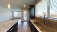 Located on Becket in Grand Prairie, TX, this single-story home offers a well-designed, open layout with quality finishes throughout. The kitchen serves as the centerpiece, showcasing dark navy shaker-style cabinetry, light granite countertops, and a tasteful subway tile backsplash. A large island provides additional prep and gathering space, while stainless steel appliances — including a refrigerator, electric range, over-the-range microwave, and dishwasher — complete the functional setup. A stainless steel undermount sink is positioned beneath a window, filling the kitchen with natural light. Wood-look plank flooring extends through the kitchen and open living area, which is bright and spacious with multiple windows and a ceiling fan overhead. A rear door offers direct outdoor access from the main living space. The bedrooms feature plush carpeting, ceiling fans, and windows with exterior views, creating comfortable, well-lit retreats. The bathroom is equipped with granite countertops, dark cabinetry, wood-look flooring, and a tiled tub/shower combination. Throughout the home, neutral wall tones and clean architectural lines create a cohesive, modern aesthetic suited for a variety of lifestyles.