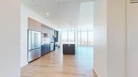 Located at 777 E Ocean Blvd in Long Beach, CA, this expansive two-floor residence offers a sophisticated high-rise living experience with seven bedrooms and three bathrooms. The open-concept kitchen and living area anchors the main floor, featuring a striking two-toned cabinetry design in blue and taupe, a large center island with quartz countertops, stainless steel appliances, a marble-style tile backsplash, and pendant lighting. Floor-to-ceiling glass windows flood the space with natural light and frame breathtaking panoramic views of the Long Beach cityscape and beyond. Light hardwood flooring runs throughout the main living areas, while bedrooms are finished with plush carpet. The spacious primary bedroom includes large windows with expansive city views and access to a dedicated bathroom suite. The primary bathroom is appointed with a dual-sink vanity, backlit mirrors, stone tile flooring, and a glass-enclosed walk-in shower with city views. Additional bathrooms maintain the same refined aesthetic with wood-tone vanities, white quartz counters, and backlit mirrors. Bedrooms feature bright, minimalist interiors with generous natural light. Sliding barn doors, structural columns, and wide hallways add architectural character throughout. An in-unit laundry closet with a full-size washer and dryer adds everyday convenience to this refined, high-rise residence.