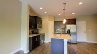 This 3-floor home features a thoughtfully designed kitchen that serves as a central highlight of the space. The kitchen showcases a central island topped with light granite countertops and an integrated sink, illuminated by elegant pendant lighting overhead. Recessed ceiling lights provide additional brightness throughout the area, complementing the warm, neutral-toned walls.

Cabinetry combines rich dark-stained lower units with lighter upper cabinets, creating a dynamic contrast that adds visual depth. A mosaic tile backsplash ties the design elements together, running along the cooking and preparation areas. Stainless steel appliances, including a French door refrigerator, electric range, and built-in microwave, add a modern, professional quality to the kitchen.

Durable hardwood-style flooring runs throughout, offering both practicality and a cohesive aesthetic. The open layout of the kitchen promotes ease of movement and functionality. Spanning three floors, this home offers generous living space, with the kitchen's refined finishes setting a high standard for the overall design and ambiance found throughout the property.
