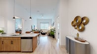 This well-appointed 2-bedroom, 2-bathroom residence offers a thoughtfully designed single-floor layout that maximizes both comfort and functionality. The open-concept kitchen and living area serves as the heart of the home, boasting soaring ceilings that create an airy, expansive atmosphere. The kitchen is outfitted with white shaker-style cabinetry, warm wood lower cabinets, granite countertops, stainless steel appliances, and a peninsula island with seating for three — ideal for casual dining and entertaining. Stylish pendant lighting accentuates the space above the island. Light wood-tone flooring flows seamlessly throughout the main living areas, while a large window at the end of the living room fills the space with natural light. The living room offers generous room for a sectional sofa and features a ceiling fan overhead. The primary bedroom is a comfortable retreat, highlighted by a bold accent wall, plush carpeting, and a bright window with garden views, along with a dedicated walk-in closet. The bathrooms feature granite-topped vanities with warm wood cabinetry and sleek black hardware. A dedicated laundry room houses a full-size washer and dryer. Together, these spaces deliver a polished, modern living experience.