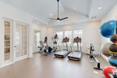 Located at 5740 Buffington Rd in Union City, GA, this fitness center is a thoughtfully designed workout facility that offers a comprehensive range of exercise equipment within a well-appointed single-room layout. The space features a vaulted tray ceiling with recessed lighting and a modern ceiling fan, creating an airy and energizing atmosphere. Durable rubber flooring covers the entire area, providing both safety and comfort during workouts.

Natural light streams in through multiple windows fitted with blinds, offering views of the surrounding outdoor area including a pool, while large wall-mounted mirrors amplify the sense of space and allow for form-checking during exercise. Elegant French doors provide access to the facility, adding an architectural touch to the clean, white interior.

The cardio section is equipped with treadmills, elliptical trainers, a stationary bike, and a rowing machine, while the strength-training area features a multi-function cable machine, adjustable benches, and a full rack of dumbbells. Functional training is supported by a TAG ball rack stocked with medicine balls, stability balls, and kettlebells, as well as a StairMaster. A bank of storage lockers provides convenient personal storage for users. This fitness center offers a complete, professional-grade workout environment.