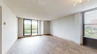 This single-floor residence on Crawford Parkway in Portsmouth, Virginia, offers a well-organized layout with a clean, neutral aesthetic throughout. The main living area is notably open and airy, finished with wood-style plank flooring that extends across the space. Large floor-to-ceiling sliding glass doors provide direct access to a private balcony, flooding the room with natural light and offering views of the surrounding greenery. Vertical blinds and additional windows allow for flexible light control.

A secondary living or dining area continues the wood-style flooring and features its own window with blinds, along with overhead lighting and a connecting hallway that leads further into the unit. The bedrooms are carpeted in a warm, neutral tone and each includes windows that bring in natural light. At least one bedroom features a closet with sliding doors and a wall-mounted light fixture, adding practical storage. Additional bedroom spaces share the same comfortable, understated character.

The bathroom is equipped with a single-sink vanity featuring white cabinetry and a laminate countertop, a tub-shower combination with tiled surround, and wood-style flooring. The overall palette throughout the residence is light and neutral, creating a cohesive and move-in-ready environment.