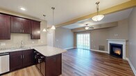 This well-appointed two-bedroom, two-bathroom residence in Buffalo, New York, offers a thoughtfully designed single-floor layout that maximizes both comfort and functionality. The open-concept kitchen and living area serves as the heart of the home, featuring rich dark wood cabinetry, granite countertops, and a large center island illuminated by elegant pendant lighting. Stainless steel appliances complete the kitchen, which flows seamlessly into the living room. The living room is a standout space, highlighted by a classic fireplace with a white mantel, gleaming hardwood-style flooring, a ceiling fan, and a sliding glass door that fills the room with natural light and offers outdoor views. The primary bedroom is generously sized, finished with plush carpeting, a ceiling fan, and a window framing outdoor scenery. The second bedroom mirrors this comfortable design. The two bathrooms are well-finished, with one featuring a granite-topped vanity with dark wood cabinetry and a full tub-shower combination, while the second offers a sleek enclosed stand-up shower. Warm neutral tones carry throughout the entire residence, creating a cohesive and inviting ambiance from room to room.