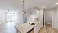 Located in the Forest Village community of Holly Springs, NC, this single-floor residence offers a clean, contemporary design throughout. The open-concept kitchen serves as the heart of the home, showcasing granite countertop surfaces, a large peninsula island with an undermount sink, white shaker-style cabinetry with sleek bar-pull hardware, and stainless steel appliances including a range, microwave, and refrigerator. Pendant lights hang above the island, adding warm, focused illumination. Wood-style luxury vinyl plank flooring runs throughout the main living areas, lending a cohesive, modern aesthetic. The living area is bright and airy, featuring a ceiling fan, recessed lighting, and French doors that invite natural light. Bedrooms are carpeted for comfort, each with ceiling fans and windows fitted with blinds. The primary bathroom features a granite-topped vanity, a large mirror with overhead lighting, wood-style flooring, and access to a walk-in closet. Additional bathrooms include a combination tub and shower. Generous closet space with wire shelving provides practical storage throughout. The neutral color palette and consistent finishes create a cohesive, move-in-ready environment well-suited for comfortable everyday living.