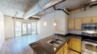 Located at 2260 Market St in Denver's vibrant Cole neighborhood, this urban loft-style unit showcases a striking industrial-chic aesthetic across a single floor. The open-concept living and kitchen area is anchored by exposed concrete ceilings with visible ductwork and track lighting, creating a raw yet refined atmosphere. Wide-plank hardwood-style flooring flows throughout the main living space, complementing the bright, airy feel enhanced by large French doors that open to street-facing views and flood the room with natural light.

The kitchen features dark granite countertops, light wood cabinetry, stainless steel appliances including a range and microwave, and a peninsula with a double stainless steel sink and elegant pendant lighting overhead. The bedroom offers plush carpeting, oversized windows with expansive city views, and a concrete ceiling that maintains the loft's cohesive industrial character.

Two bathrooms are finished with tile flooring, granite-topped vanities, and light wood cabinetry; one includes a tiled soaking tub and shower combination. A dedicated laundry room with a full-size washer and dryer adds everyday convenience. This well-appointed unit balances urban edge with functional comfort in the heart of Denver.