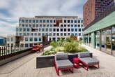Located at 1070 Bridgeview Way in San Francisco's Mission Bay neighborhood, this two-floor amenity space is defined by its generous outdoor terraces and thoughtfully designed communal areas. The exterior facade is clad in distinctive sage-green tile, lending the building a modern and refined aesthetic that stands out amid the surrounding urban landscape.

Across both levels, multiple open-air terraces provide a variety of outdoor experiences. Landscaped planter beds filled with ornamental grasses, succulents, and flowering shrubs create natural focal points throughout the space. Seating areas are furnished with contemporary lounge chairs, sofas, and dining sets in bold accent colors, offering spaces for both relaxation and social gatherings. An outdoor grilling station with bar-height seating adds a functional entertaining element to one of the terraces.

Interior lounge areas, visible through floor-to-ceiling sliding glass doors, connect seamlessly to the outdoor terraces and feature an open, well-lit layout. The terrazzo-finished terrace flooring adds a polished, durable surface underfoot.

Elevated vantage points offer panoramic views of the Mission Bay skyline, Oracle Park, and the broader San Francisco cityscape, making the outdoor terraces a standout feature of the space. A dedicated walkway lined with lush plantings further enhances the connection between nature and the built environment.