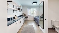 Located at 622-626 Third Ave S in Nashville, TN, this compact studio unit is a masterclass in efficient, modern design. The single-floor layout maximizes every inch of space with a clean, contemporary aesthetic defined by crisp white walls, polished concrete floors, and striking black hardware accents throughout.

The kitchenette runs along one wall and features white cabinetry with matte black pulls, a dark countertop, an integrated sink, and open shelving with black bracket supports — providing ample storage and workspace. A microwave and compact appliances are neatly incorporated into the shelving system, keeping the area functional and organized.

The sleeping area accommodates a full-sized bed and includes a large full-length mirror framed in black, enhancing the sense of space. A window with horizontal blinds allows natural light to filter in, offering a view of greenery outside. A wall-mounted mini-split unit ensures climate control.

The bathroom is tiled in neutral tones and features a toilet, towel bar, and toilet paper holder in a coordinating matte black finish, maintaining design consistency. A dedicated closet with hanging space adds practical storage.

This unit delivers a streamlined, modern living experience suited for individuals seeking smart, no-frills accommodations in Nashville.