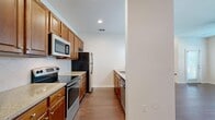 This single-story home offers four bedrooms, two bathrooms, and a functional layout designed for comfortable everyday living. The open-plan living room is a standout space, featuring rich hardwood-style flooring, multiple windows fitted with horizontal blinds, and a ceiling fan that fills the room with natural light and airflow. A louvered door near the kitchen entry adds a classic architectural detail.

The kitchen runs along a galley-style corridor with warm wood cabinetry, granite-style countertops, a tile backsplash, and a full suite of stainless steel appliances including a range, microwave, refrigerator, and dishwasher. A peninsula with pendant lighting connects the kitchen to the living area, enhancing the open feel.

The four bedrooms are carpeted and include ceiling fans; the primary bedroom offers a modest but practical footprint. Three closets provide ample storage throughout. Both bathrooms include tile flooring, wood vanity cabinetry with granite countertops, and a tub-shower combination. A dedicated laundry room with washer and dryer hookups adds everyday convenience. The overall aesthetic is clean, neutral, and move-in ready.