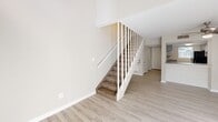 This two-story residence in Birmingham, Alabama offers a practical and well-organized layout across two floors. The main level opens into a bright, airy living room featuring light wood-style flooring, a ceiling fan, and built-in shelving that adds functional character to the space. A carpeted staircase with white balustrades rises from the living area, complementing the home's clean, neutral palette. The galley-style kitchen is efficiently designed, offering gray cabinetry, laminate countertops, a double stainless steel sink, and black appliances, including a full-size refrigerator. A window above the sink allows natural light to brighten the workspace. A hallway on the main floor provides access to the bathroom and a closet, keeping the layout organized and accessible. The bathroom is straightforward and functional, featuring a tub-shower combination with tiled surround, a toilet, and a vanity, with a window providing natural ventilation and light. Upstairs, the second floor is carpeted and offers open, flexible bedroom space with sloped ceiling details and a window that draws in natural light. The upper level's loft-like quality lends versatility to the sleeping quarters. Throughout, the home maintains a consistent neutral tone with light walls and trim, creating a clean and cohesive atmosphere.