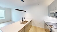 This well-appointed one-bedroom, one-bathroom unit at 500 Maury offers a thoughtfully designed single-floor layout with a clean, modern aesthetic throughout. Light wood-tone flooring flows seamlessly across the entire space, creating a warm and cohesive feel.

The contemporary kitchen serves as a functional centerpiece, featuring sleek gray cabinetry, white quartz countertops, and a full suite of stainless steel appliances including a refrigerator, range, and built-in microwave. A striking black linear pendant light hangs above the kitchen island, which includes an undermount stainless steel sink with a matte black faucet — adding a refined, modern contrast to the bright white surfaces.

The bedroom is comfortably sized and filled with natural light from a window overlooking the surrounding building exterior. A ceiling fan provides year-round comfort, and the room's crisp white walls enhance the sense of openness.

A dedicated laundry area with a stacked washer and dryer unit adds everyday convenience, situated adjacent to the bathroom. The bathroom features a vanity with gray cabinetry, a backlit mirror, and clean tile flooring, maintaining the modern design language found throughout the home.

The overall ambiance is bright, minimalist, and move-in ready, with a consistent palette of white walls, light floors, and contemporary fixtures.