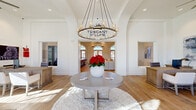 The Tuscany Villas leasing office at 6710 W Doe Ave in Visalia, California, presents an architecturally refined single-story space designed to make a lasting first impression. Upon entry, visitors are greeted by a dramatic foyer with soaring ceilings and a striking circular chandelier suspended above a round central table, setting an elegant and welcoming tone. The Tuscany Villas branding is prominently displayed on the wall, reinforcing the community's identity.

The interior is unified by warm-toned hardwood flooring that extends throughout, complementing the crisp white walls and bright, airy atmosphere. Signature arched windows fitted with plantation shutters are a defining architectural feature, allowing abundant natural light to pour into every area of the space. The main gathering area is generously proportioned, accommodating multiple seating arrangements with neutral-toned sofas, accent chairs, and low coffee tables arranged to encourage comfortable conversation.

Lush indoor plants, including tall fiddle-leaf fig trees, add organic warmth and visual interest throughout. Carefully chosen artwork and décor accessories contribute to the space's polished yet approachable aesthetic. The layout flows openly between zones, supported by arched doorways that echo the window design and reinforce the cohesive architectural language throughout this welcoming community office.