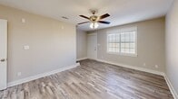 Located at 1214 Bradley Bowen Drive in Valdosta, GA, this two-story home offers a well-organized layout spread across two floors. The main level features an open-concept living, dining, and kitchen area bathed in natural light from plantation-shuttered windows. The kitchen is outfitted with white shaker-style cabinetry, gleaming white countertops, a peninsula sink, and a full suite of stainless steel appliances including a refrigerator, range, and microwave. Wood-look plank flooring runs throughout, lending a clean, cohesive aesthetic to the space. A staircase with white risers, gray treads, and a sleek metal handrail connects the two floors, with a pantry conveniently positioned at the top landing. The main level also includes a laundry area, utility spaces, a patio, and a bathroom. Upstairs, two bedrooms each feature ceiling fans, closets, and continued wood-look flooring. The primary bedroom is generously proportioned with its own dedicated closet space. Two additional bathrooms on the upper level include tub-shower combinations and clean white vanities with brushed nickel fixtures. The home also includes an office and multiple hallways for easy circulation. Outside, a newly constructed cedar privacy fence encloses the backyard, offering a secure outdoor retreat.