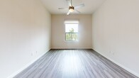 Located along NASA Parkway in Houston, TX, this well-appointed one-bedroom, one-bathroom unit offers a thoughtfully designed single-floor layout. The combined kitchen and living area forms the heart of the home, featuring durable luxury vinyl plank flooring, soaring ceilings, and pendant lighting that adds a modern touch. The kitchen is equipped with dark espresso cabinetry reaching near the ceiling, granite countertops, a tile backsplash, stainless steel appliances including a gas range, built-in microwave, and a French door refrigerator, all centered around a peninsula with a built-in sink. The open living area flows naturally from the kitchen, bathed in natural light. The bedroom is generously sized, finished with plush carpet, a ceiling fan, and large sliding glass doors that open to a private balcony with ornate ironwork railings and lush outdoor views. Two closets provide ample storage, including a spacious walk-in closet outfitted with wire shelving. The bathroom is a standout feature, showcasing floor-to-ceiling marble-style tile, a glass-enclosed walk-in shower, granite vanity countertop, and elegant finishes throughout. A hallway connects the living spaces with clean, neutral tones maintained throughout the unit.
