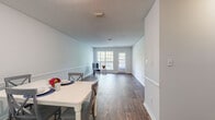This two-bedroom apartment at Bell Oaks Apartments in Montgomery, Alabama offers a clean, functional layout spread across a single floor. The open-concept living and dining area is one of the unit's most notable features, characterized by warm wood-style plank flooring that runs throughout, crisp white walls with a chair rail detail, and a set of glass-paneled doors at the far end that invite natural light deep into the space. The generous proportions of this combined area provide ample room for both dining and living arrangements.

The kitchen is efficiently designed in a galley configuration, featuring white cabinetry, granite-style countertops, white appliances including a refrigerator, electric range, and dishwasher, along with a double-basin sink. The layout maximizes storage and counter space throughout.

Each bedroom is well-sized, finished with the same wood-style flooring and equipped with a ceiling fan and a closet with bifold doors. The bathrooms mirror the kitchen's aesthetic with white cabinetry, granite-style countertops, and large vanity mirrors. One bathroom features a shower-tub combination, offering practical everyday functionality throughout the residence.