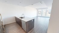 Located on the 11th floor at 425 5th Avenue SE in the heart of downtown Calgary, this modern one-bedroom, one-bathroom unit offers a well-designed open-concept layout with clean finishes throughout. Light hardwood-style flooring runs consistently across the living areas, complementing the bright, white walls and creating a cohesive, contemporary aesthetic.

The open-concept kitchen is a standout feature, showcasing a large island with a striking marble-look quartz countertop, dark wood cabinetry, and stainless steel appliances including a refrigerator, gas range, built-in oven, and microwave. The island provides both additional prep space and an integrated sink, making it as functional as it is visually appealing.

The living room is bathed in natural light through floor-to-ceiling windows that frame sweeping views of the Calgary skyline, giving the space an open, airy feel. The bedroom also benefits from large windows with access to a balcony, offering more city views and abundant natural light. A built-in sliding closet adds practical storage.

The bathroom features elegant marble-tiled walls surrounding a soaker tub with a handheld shower, lending a refined, spa-like quality to the space. Overall, this unit combines modern design with a prime urban location.
