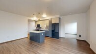 Located at 1201 Mercer St in Seattle's South Lake Union neighborhood, this 2-bedroom, 2-bathroom residence offers a well-designed, single-level floor plan with a clean, contemporary aesthetic throughout. The open-concept living, dining, and kitchen area serves as the heart of the home, anchored by a sleek kitchen featuring two-tone cabinetry in dark gray and crisp white, a textured tile backsplash, white quartz countertops, black stainless steel appliances, and a central island with pendant lighting — ideal for both cooking and casual dining. Hardwood-style flooring flows through the main living areas, adding warmth and continuity. The living room receives generous natural light through a large sliding glass door. Both bedrooms are carpeted and well-proportioned, with the primary bedroom offering a notable sense of space and direct access to a full bathroom with dark wood vanity cabinetry. The secondary bedroom is served by a second full bathroom featuring a tub/shower combination and tile flooring. Three closets provide practical storage throughout. A hallway connects the private and shared spaces efficiently, and the overall layout makes excellent use of the available square footage.
