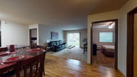 Located at 215 32nd Street East in Williston, North Dakota, this single-floor unit offers a well-designed, open-concept layout that seamlessly connects the main living areas. Warm hardwood-style flooring flows throughout the kitchen and dining areas, creating a cohesive and inviting atmosphere.

The kitchen is equipped with light maple cabinetry, dark granite-style countertops, and black appliances including a range, microwave, and refrigerator. A peninsula with an overhang provides additional workspace and casual seating, while a dedicated dining area nearby accommodates a full dining set. 

The living room transitions to soft carpeting and is anchored by a large sliding glass door fitted with vertical blinds, allowing ample natural light and providing direct access to an outdoor view of a green lawn. A wall-mounted air conditioning unit is also present for climate control.

Two bedrooms are accessible via a central hallway, each featuring carpet flooring, a ceiling fan, a window with blinds for natural light, and sufficient space for full bedroom furnishings. The full bathroom is conveniently located off the hallway and includes a shower/tub combination, toilet, and vanity with wood cabinetry, all set on hardwood-style flooring. The overall ambiance of the unit is practical and comfortable.