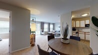 This single-floor residence offers a thoughtfully designed open-concept layout that seamlessly connects the living, dining, and kitchen areas. The living room is generously sized, featuring plush wall-to-wall carpeting, neutral walls, and large windows with patterned drapes that invite abundant natural light. A pass-through window connects the living area to the kitchen, enhancing the sense of openness throughout.

The dining area accommodates a round wooden table with modern upholstered chairs and is accented by a bold abstract wall piece, creating an inviting space for everyday meals or entertaining. The kitchen features wood-trimmed cabinetry with white panel inserts, a subway tile backsplash, white appliances including a range and dishwasher, and durable wood-look flooring that adds warmth to the space.

The residence includes two well-proportioned bedrooms, each carpeted and filled with natural light from sizable windows fitted with horizontal blinds. The bathroom features a full tub-shower combo, a wood-trimmed vanity with an integrated sink, and clean, bright finishes. A dedicated in-unit laundry room houses a full-sized washer and dryer with open shelving above for added storage. Throughout, the space maintains a clean, modern aesthetic with a warm, neutral palette.