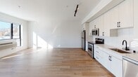Located at 3701 Stinson Blvd in St. Anthony, Minnesota, this single-floor unit showcases a clean, contemporary design defined by bright white walls, light wood-tone flooring, and black hardware accents carried consistently throughout the space. The open-concept layout connects the living area to the kitchen, creating a generous, airy feel enhanced by track lighting overhead.

The kitchen is well-appointed with white shaker-style cabinetry extending to the ceiling, a subway tile backsplash, light countertops, and stainless steel appliances including a refrigerator, electric range, and over-the-range microwave. A matte black faucet paired with a copper-toned undermount sink adds a distinctive design detail.

The living and sleeping areas feature large, black-framed windows that draw in abundant natural light and provide outdoor views of the surrounding St. Anthony neighborhood. Ceiling fans are installed in the bedroom areas, contributing to year-round comfort alongside wall-mounted PTAC climate control units.

The bathroom continues the unit's cohesive aesthetic with white cabinetry featuring black hardware, a combined tub and shower, and wood-tone flooring that ties back to the rest of the space. Overall, the unit presents a modern, move-in-ready environment with consistent finishes and a bright, open atmosphere.