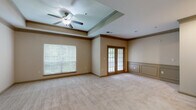 Located at 100 Stonecrest Blvd in Stonecrest, Georgia, this single-floor residence offers a thoughtfully designed layout with a range of notable architectural details throughout. The spacious main living area is a standout feature, showcasing an elegant tray ceiling accented with crown molding and equipped with a ceiling fan. Large windows flood the room with natural light, offering views of the surrounding greenery, while classic French doors with divided lite glass panes provide both style and access. Decorative wainscoting adds a refined touch to the living space walls. The kitchen is well-appointed with rich cherry-toned cabinetry, a tile backsplash, black appliances including a range, dishwasher, and refrigerator, and a central island that provides additional prep and storage space. Light tile flooring ties the kitchen together seamlessly. The bedrooms feature soft, neutral-toned carpeting and windows that bring in natural light, maintaining a calm and comfortable atmosphere. A bathroom includes a soaking tub and shower combination with tasteful diamond-pattern tile accents. Throughout the residence, warm neutral wall tones and consistent trim details create a cohesive and inviting ambiance.