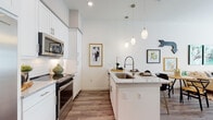 This thoughtfully designed single-floor residence offers a seamless blend of modern finishes and comfortable living spaces. The open-concept kitchen is a standout feature, showcasing crisp white shaker cabinetry, a white subway tile backsplash, granite countertops, and a generously sized island with a built-in sink and bar seating. Stainless steel appliances, including a side-by-side refrigerator, electric range, and over-the-range microwave, complete the space. Elegant pendant lighting hangs above the island, adding warmth to the bright, airy atmosphere. Wood-look flooring flows throughout the main living areas, lending a cohesive and polished look.

The living area provides a welcoming retreat with tall ceilings and ample space for entertaining, while the adjacent dining nook offers a cozy setting just off the kitchen. The bedroom features plush carpeting, generous natural light through large windows with blinds, and a calm, neutral palette. The en-suite bathroom is particularly impressive, with a long double-vanity topped with granite, wide-format tile flooring, large-format wall tile, and a glass-enclosed walk-in shower. A closet area adjacent to the bathroom adds practical storage. Throughout the space, clean lines, neutral tones, and quality finishes create an inviting and contemporary living environment.